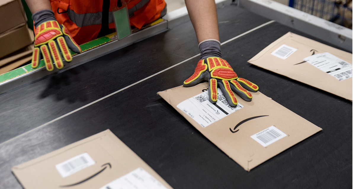 A person wearing gloves and a safety vest places brown envelopes on a conveyor belt. 