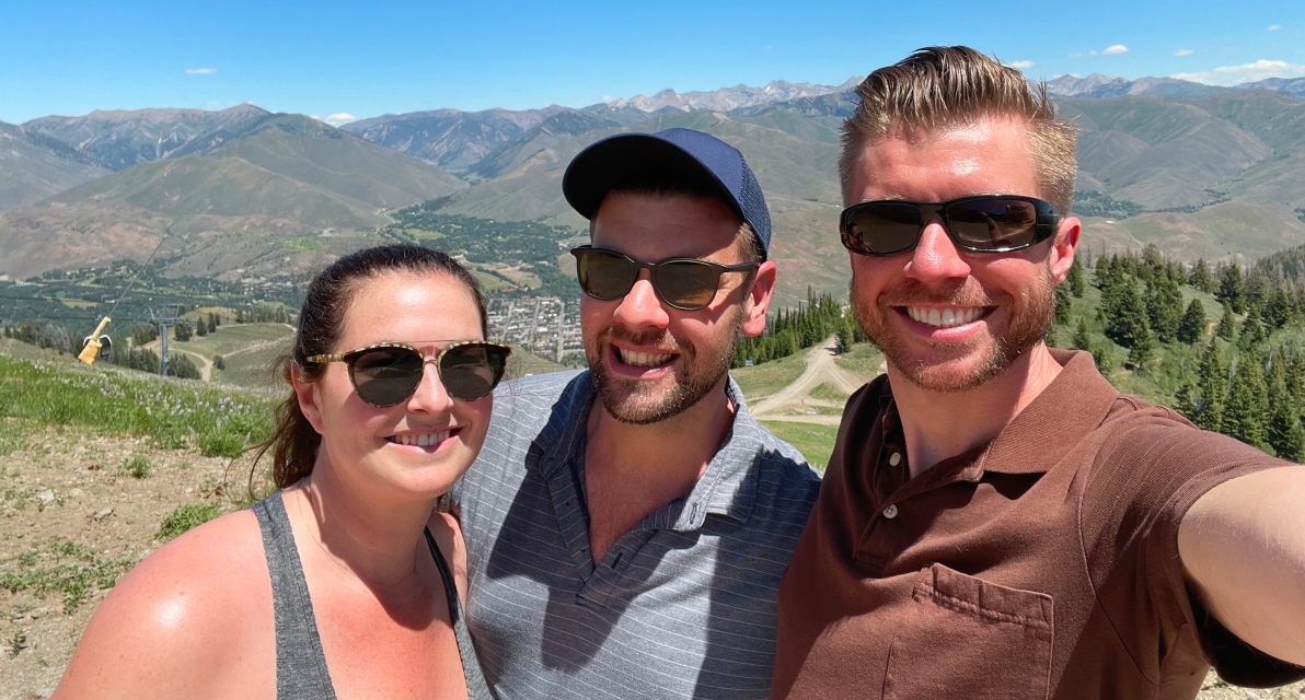 Three people wearing sunglasses smile for a photo. 