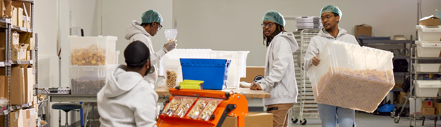 A group of people wearing hair nets sort products into bags and bins.